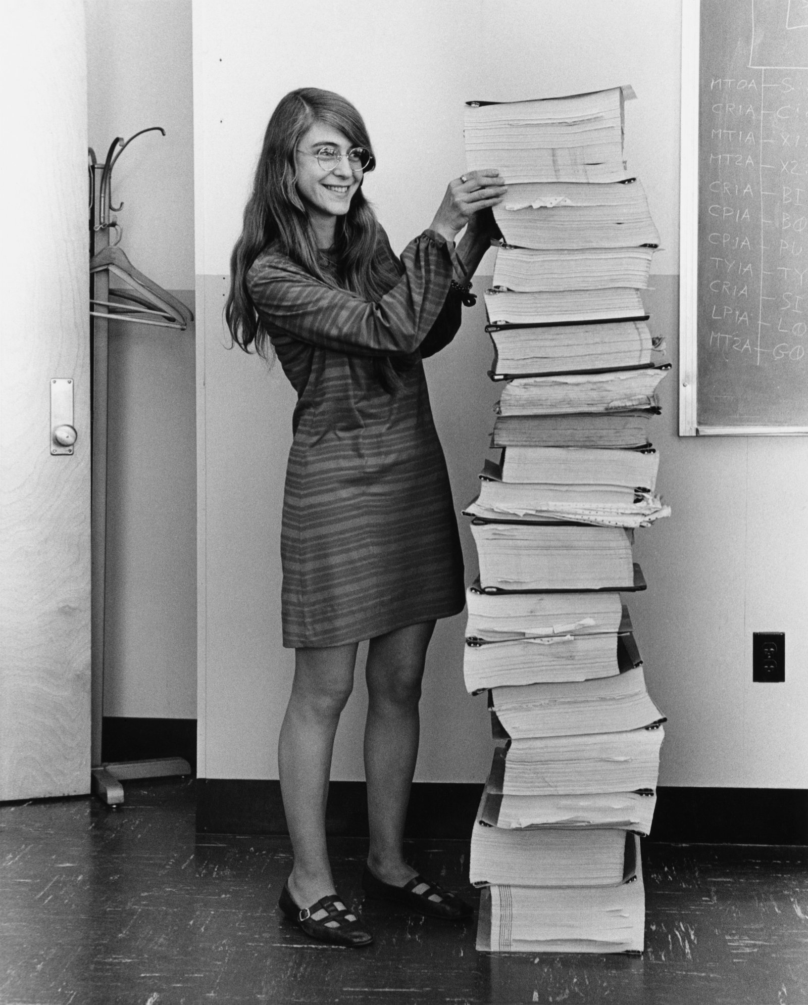 Margaret Hamilton standing next to a stack of Apollo guidance software printouts, 1969. She coined the term "software engineering." Before Apollo, she programmed Edward Lorenz's weather simulations on the LGP-30 at MIT. NASA, public domain.