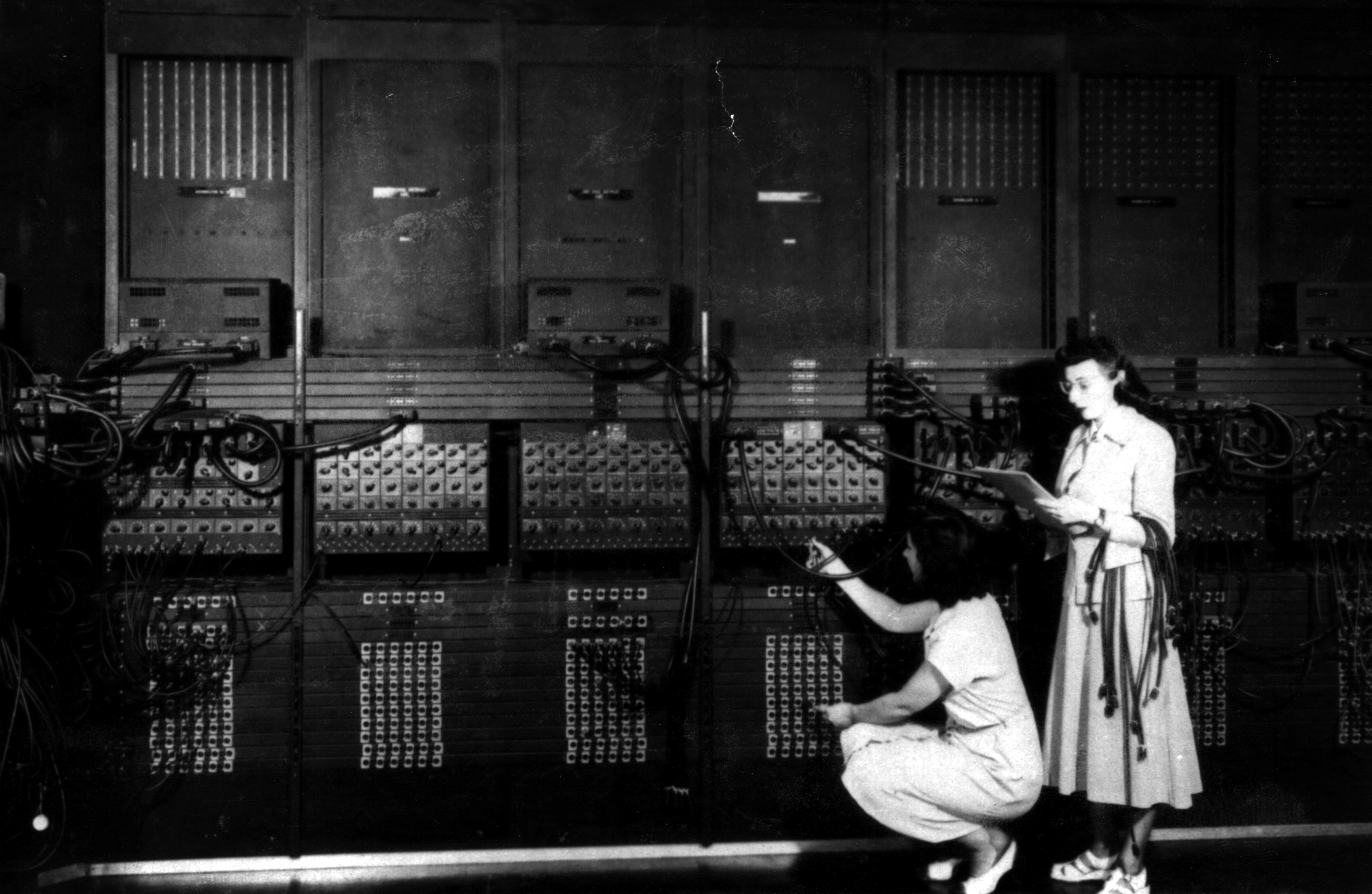Two women wiring the right side of the ENIAC with a new program, in the "pre-von Neumann" days. Standing: Ester Gerston. Crouching: Gloria Gordon Bolotsky. Public Domain: U.S. Army Photo, ARL Technical Library, 1946.